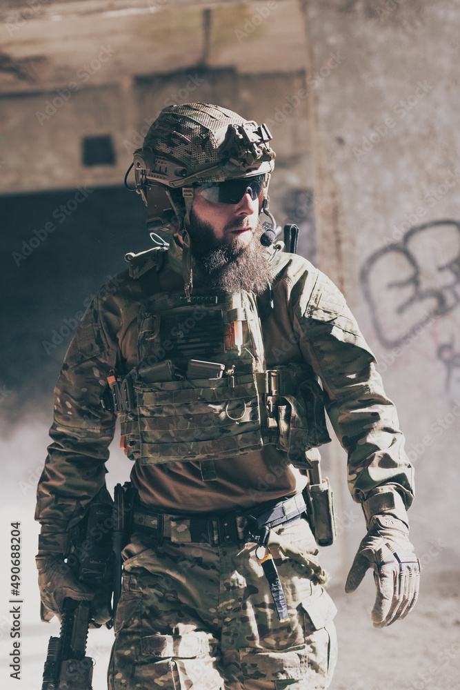 Fototapeta premium A bearded soldier in a special forces uniform walks through an abandoned building after a successful mission. Selection focus 