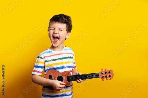 funny boy playing guitar. A child with a guitar on a yellow background in the studio. Emotions. The child emotionally plays the guitar and sings