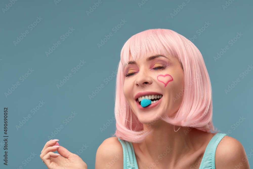 Close up of a flirtatious female model with a candy in mouth. Pretty glamorous woman pink hair charm sweets lifestyle enjoyment sugar Close up of a flirtatious female model with a candy in mouth. Pretty glamorous woman pink hair charm sweets lifestyle enjoyment sugar