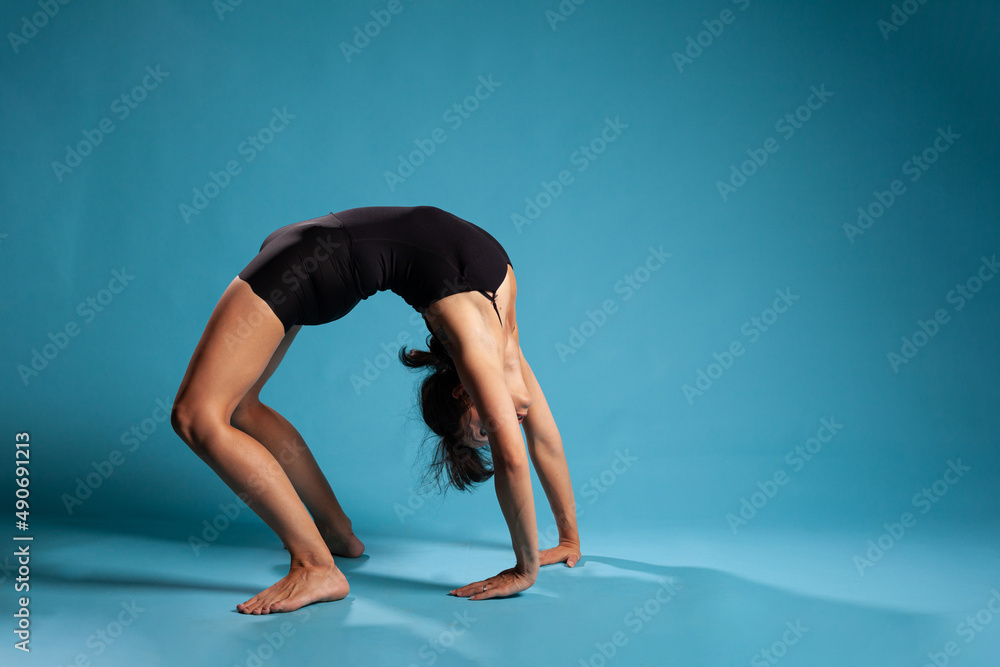 Trainer woman doing urdhva dhanurasana exercise in studio with blue background. Fit active person stretching body muscles working at healthy lifestyle. Bridge pose concept