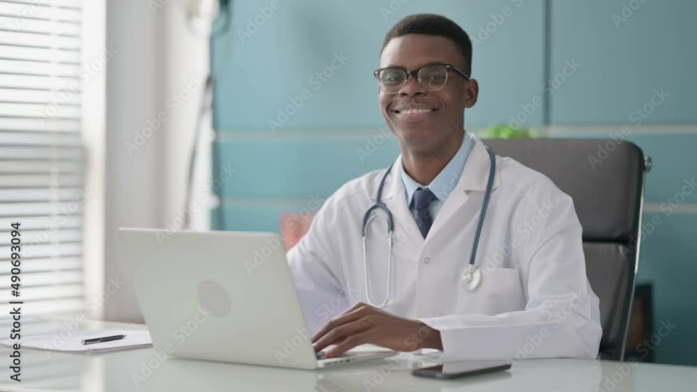Young African Doctor Smiling at Camera while using Laptop in Office Young African Doctor Smiling at Camera while using Laptop in Office