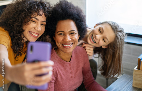 Happy african american mother and teen daughters using smartphone apps for shopping social media
