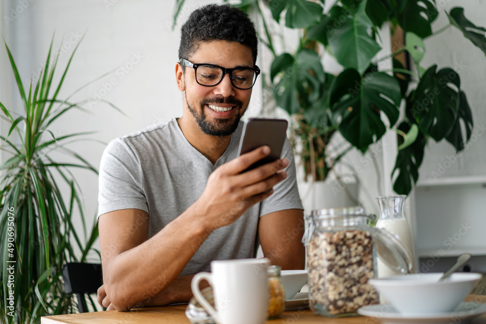 Young black man eating breakfast and reading the news online. Handsome man using mobile phone Young black man eating breakfast and reading the news online. Handsome man using mobile phone