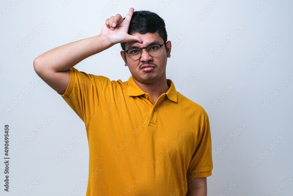 Young handsome man making fun of people with fingers on forehead doing loser gesture mocking and insulting. Young handsome man making fun of people with fingers on forehead doing loser gesture mocking and insulting.