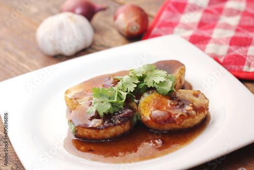 Egg with Tamarind Sauce in a white plate served on a wooden table with coriander sprinkles, is a popular local dish that Thai people eat.