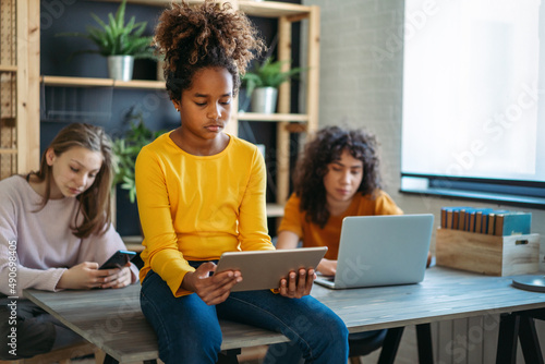 Diverse ethnicity student girls, sisters using a digital gadgets, having fun or studying together.