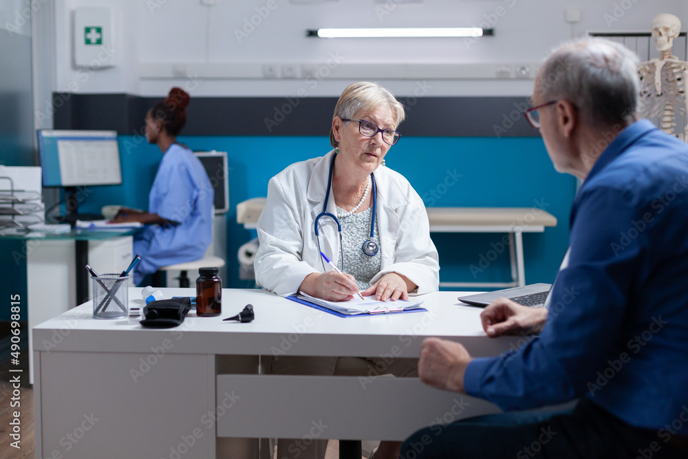Obraz premium Medic signing clipboard document and doing medical consultation with patient. Woman doctor writing checkup papers to give prescription medicine to senior man at healthcare appointment.