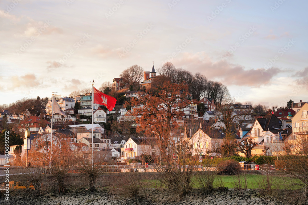 Blankenese in the city of Hamburg, northern Germany. One of Hamburg’s most affluent neighborhoods. Sunset townscape view with Süllberg, famous hill in Blankenese and flag of Hamburg.