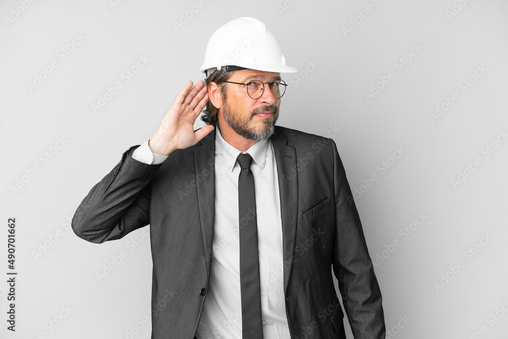 Young architect man with helmet over isolated background listening to something by putting hand on the ear Young architect man with helmet over isolated background listening to something by putting hand on the ear