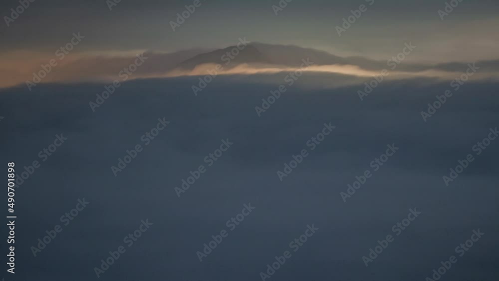 Aerial timelapse of dense layer of clouds passing between mountain tops at blue hour in Kowloon Peak, Hong Kong, China