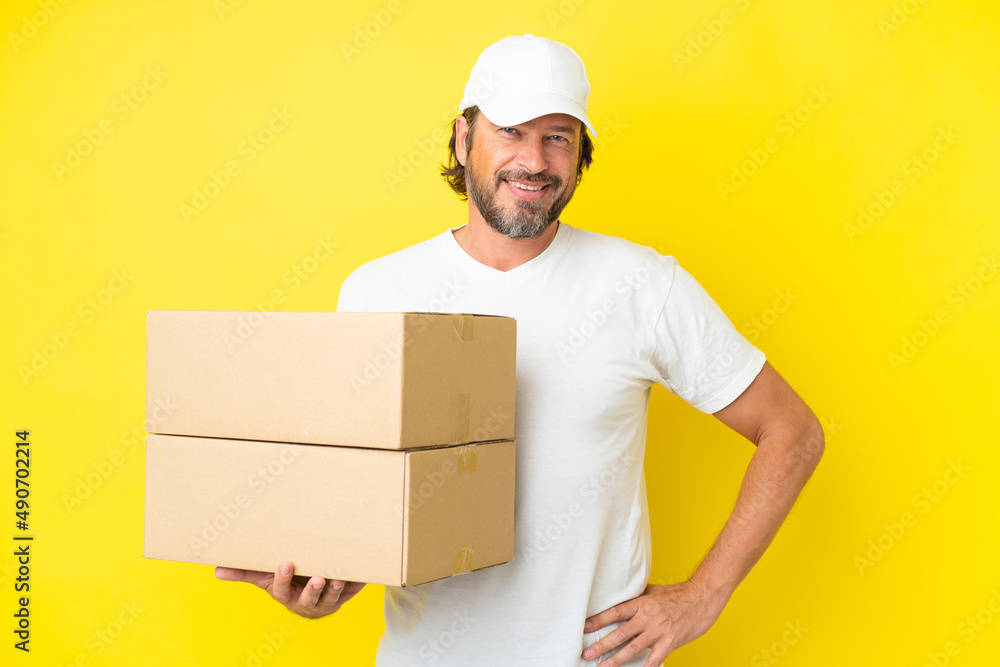Delivery senior dutch man isolated on yellow background posing with arms at hip and smiling Delivery senior dutch man isolated on yellow background posing with arms at hip and smiling