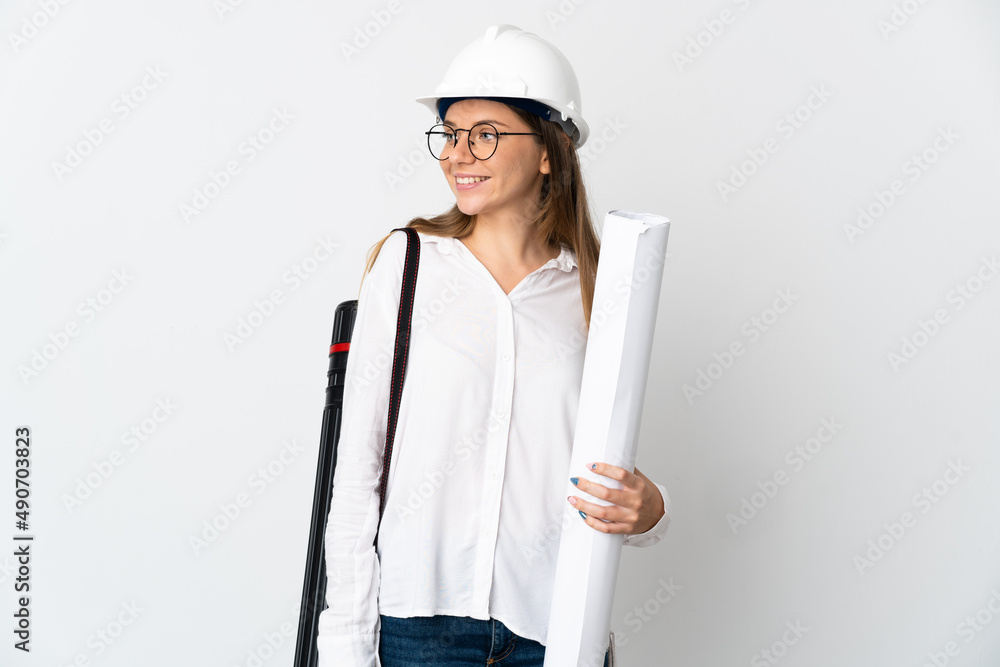 Young Lithuanian architect woman with helmet and holding blueprints isolated on white background looking to the side and smiling Young Lithuanian architect woman with helmet and holding blueprints isolated on white background looking to the side and smiling