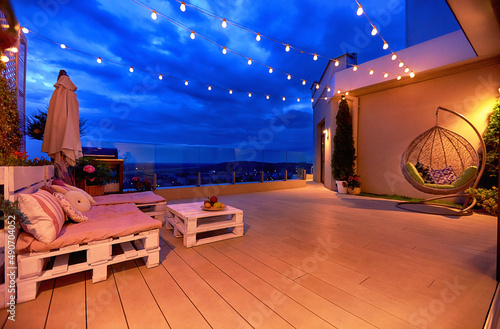 cozy rooftop patio area with lounge zone, hanging chair and and string lights at warm summer evening photo