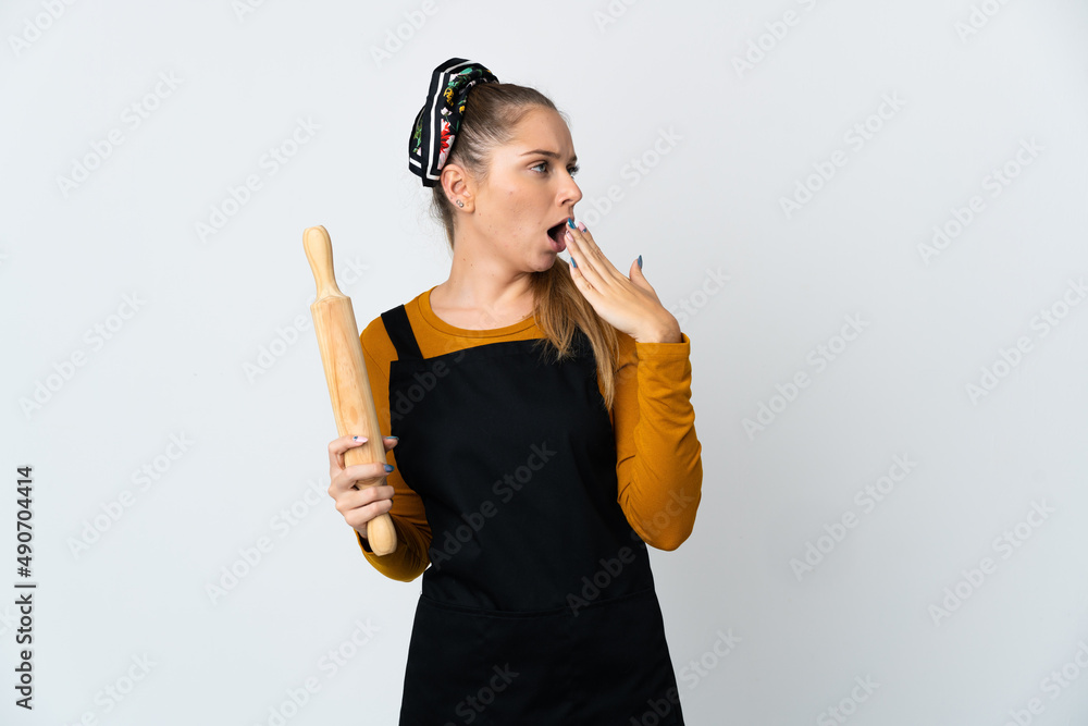 Young Lithuanian woman holding a rolling pin isolated on white background yawning and covering wide open mouth with hand Young Lithuanian woman holding a rolling pin isolated on white background yawning and covering wide open mouth with hand