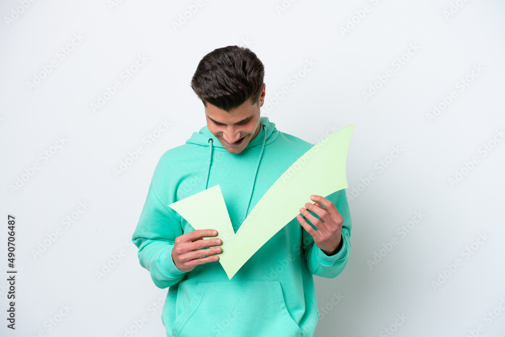 Young handsome caucasian man isolated on white bakcground holding a check icon and looking it Young handsome caucasian man isolated on white bakcground holding a check icon and looking it