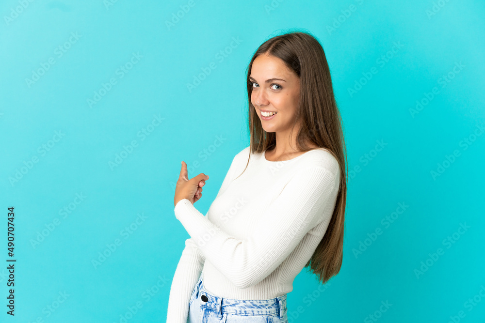 Fototapeta premium Young woman over isolated blue background pointing back