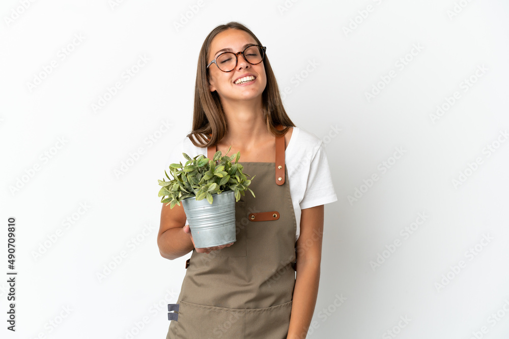 Gardener girl holding a plant over isolated white background laughing Gardener girl holding a plant over isolated white background laughing