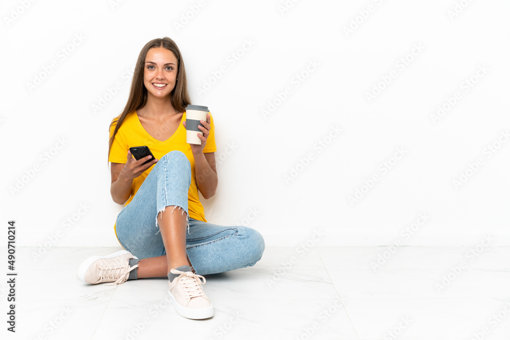 Young girl sitting on the floor holding coffee to take away and a mobile Young girl sitting on the floor holding coffee to take away and a mobile