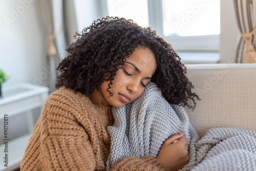 Sick young african woman feeling cold covered with blanket sit on bed, ill black girl shivering freezing warming at home wrapped with plaid, no central heating problem, fever temperature flu concept