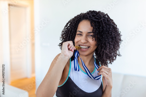Portrait of playful young female runner smiling aside and biting her gold medal . Sports, active lifestyle, motivation concept photo