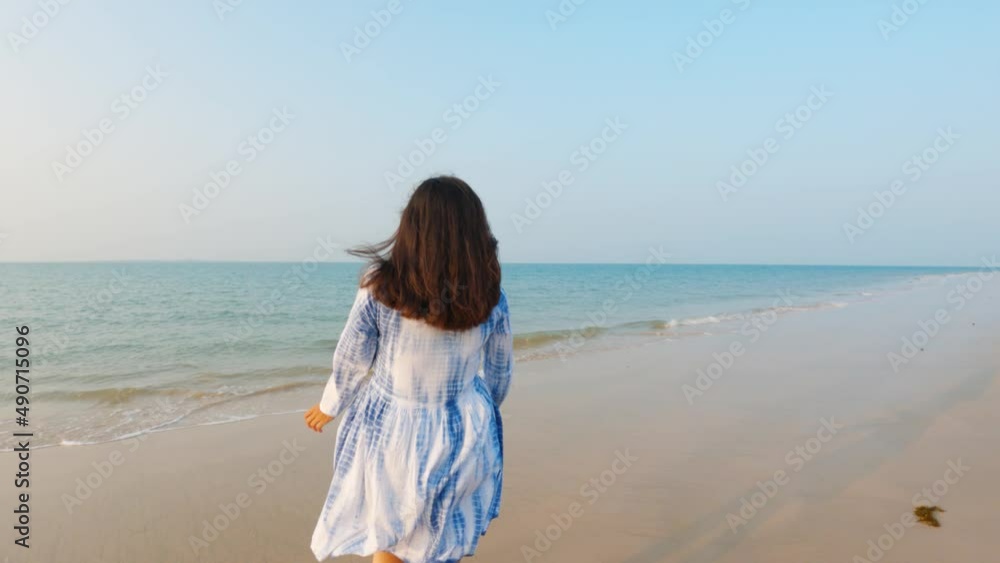 Beautiful young Indian woman in white dress walking to the sea and raising arms. Female enjoying at beach during sunset in vacation trip. Holiday and travel concept. Beautiful young Indian woman in white dress walking to the sea and raising arms. Female enjoying at beach during sunset in vacation trip. Holiday and travel concept.