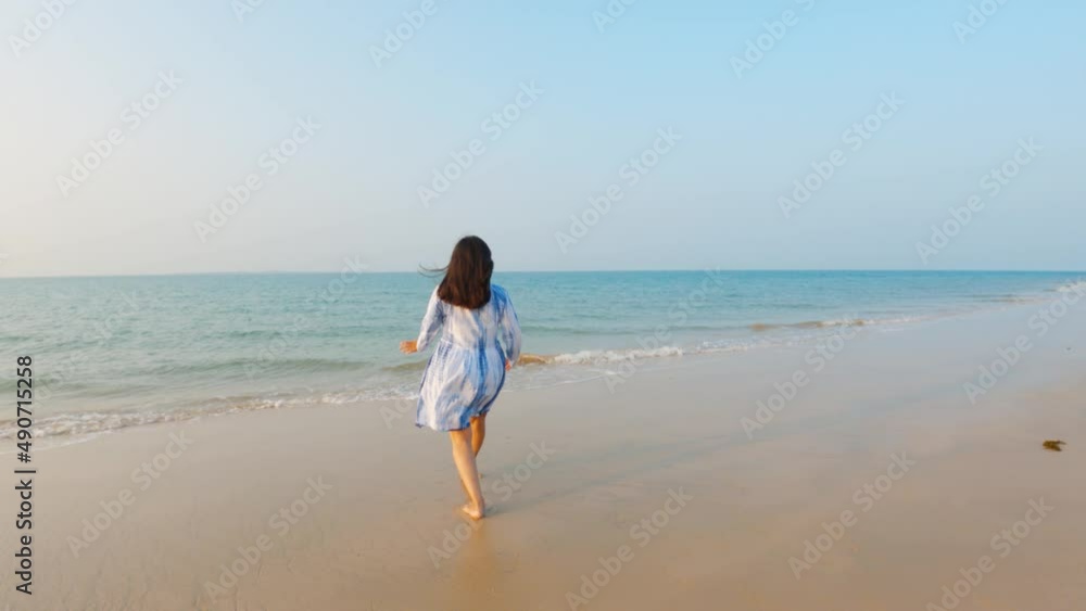 Beautiful young Indian woman in white dress walking to the sea and raising arms. Female enjoying at beach during sunset in vacation trip. Holiday and travel concept. Beautiful young Indian woman in white dress walking to the sea and raising arms. Female enjoying at beach during sunset in vacation trip. Holiday and travel concept.