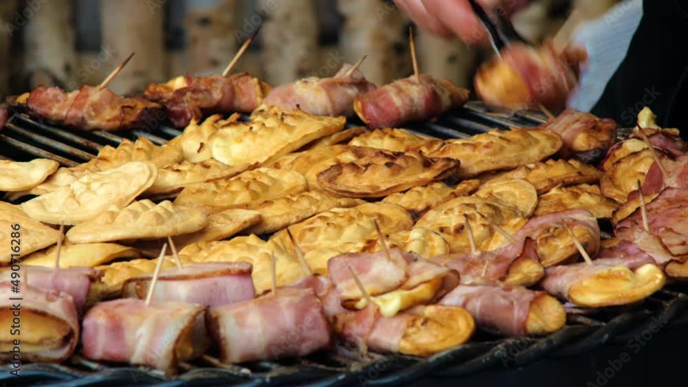 Woman preparing lots of variation on traditional Polish oscypek with melted cheese and bacon on an outside grill, bbq, oscypki being prepared. Street food warm delicious traditional regional snack Woman preparing lots of variation on traditional Polish oscypek with melted cheese and bacon on an outside grill, bbq, oscypki being prepared. Street food warm delicious traditional regional snack