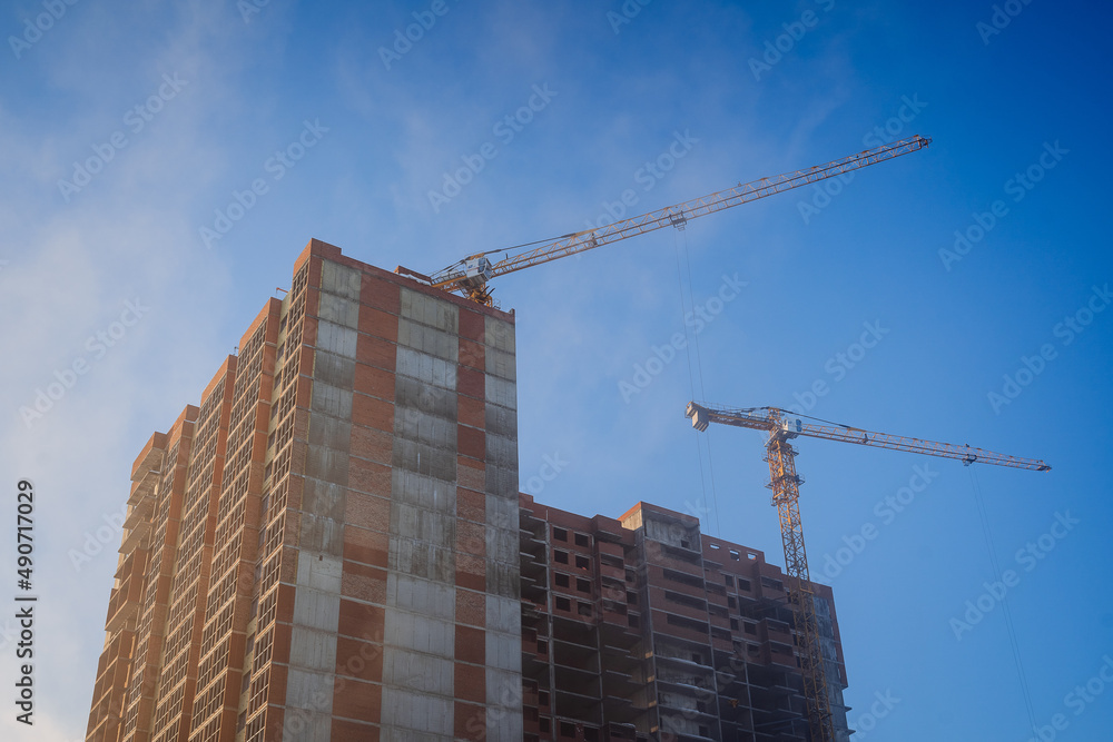 Construction of a residential building against the background of a blue sky. Construction cranes lift the load.
