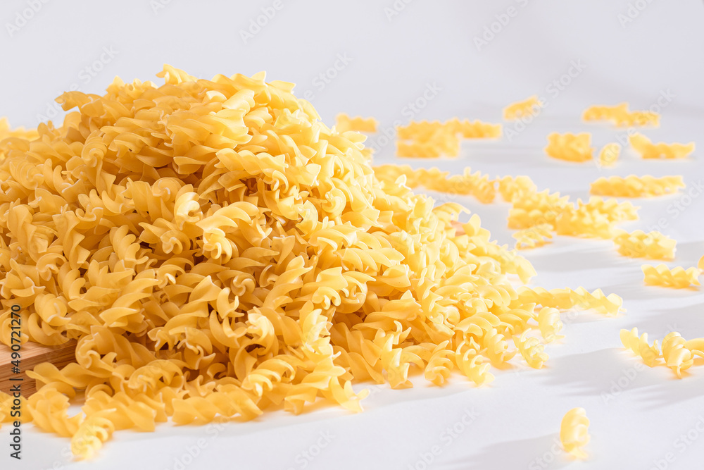 Uncooked Fusilli Pasta Scattered on Wooden Board and White Table. Raw and Dry Macaroni. Fat and Unhealthy Food Uncooked Fusilli Pasta Scattered on Wooden Board and White Table. Raw and Dry Macaroni. Fat and Unhealthy Food