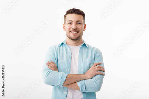 Portrait of a cheerful young man in a white T-shirt on a white background. The guy is standing looking at the camera and smiling. © Aleksandr Rybalko