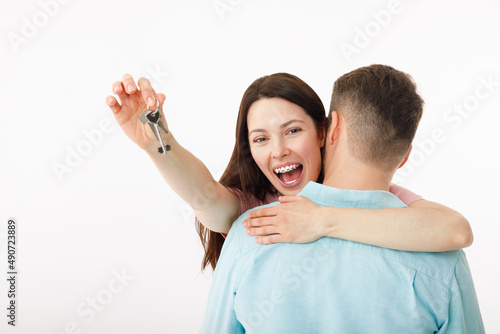 A cheerful young couple is hugging in the kitchen, holding the keys to a new house in their hands. Happy newlyweds moved into a new apartment, got a mortgage, moving day.