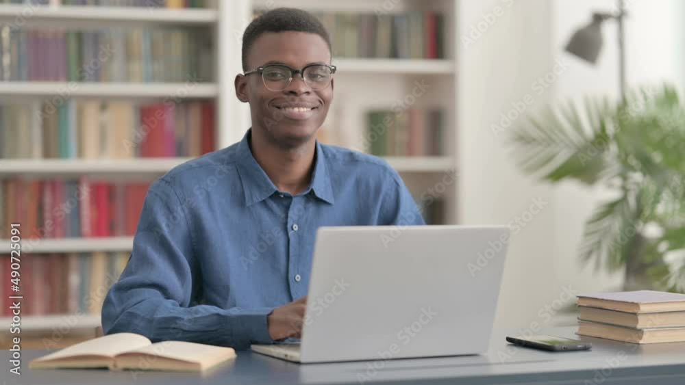 Young African Man Smiling at Camera while using Laptop Young African Man Smiling at Camera while using Laptop