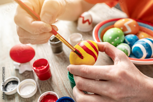 Hand with a brush is drawing a colored pattern on an Easter egg. Preparation for the bright Easter holiday
