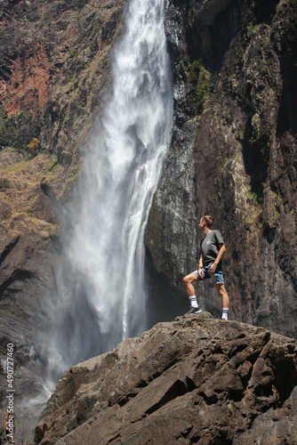 long hair man facing a huge waterfall in Australia