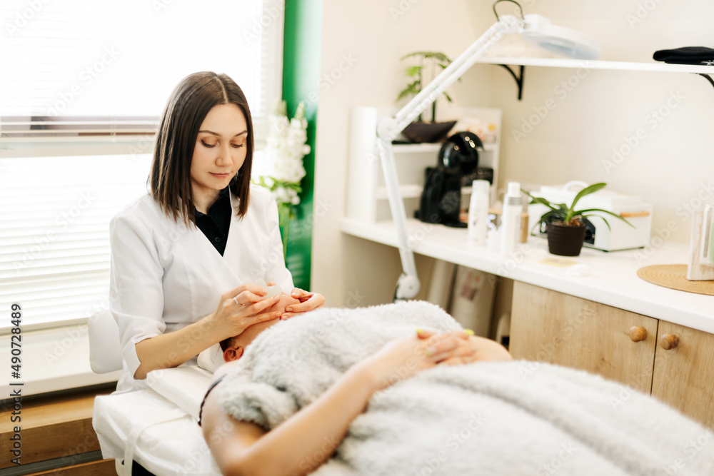 A cosmetologist massages the skin of a young woman with a gouache scraper. Facial massage, skin care, treatments A cosmetologist massages the skin of a young woman with a gouache scraper. Facial massage, skin care, treatments