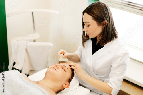 A cosmetologist massages the skin of a young woman with a gouache scraper. Facial massage, skin care, treatments