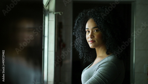 A contemplative young woman standing by window looking outside