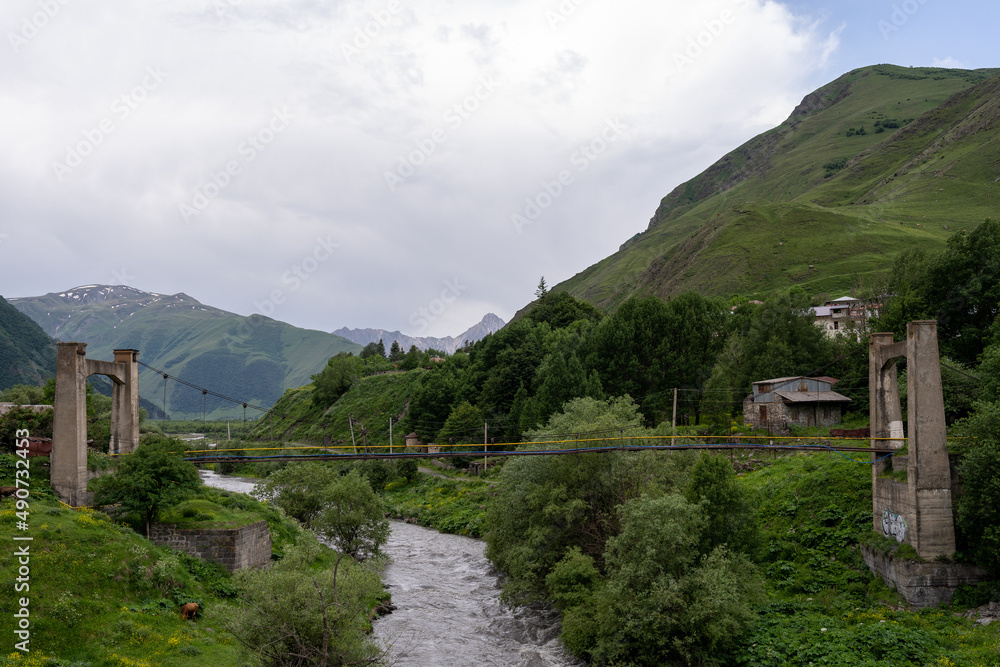 a small river in a mountain valley over which a bridge runs, where green trees and grass have disappeared along both sides.