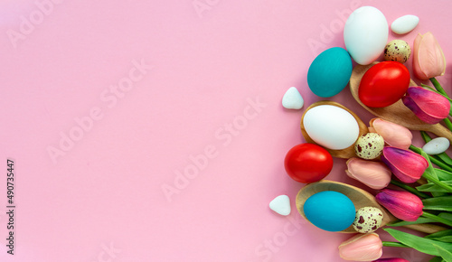 Easter background with colored Easter eggs on pink and spring tulip flowers. Top view with copy space 