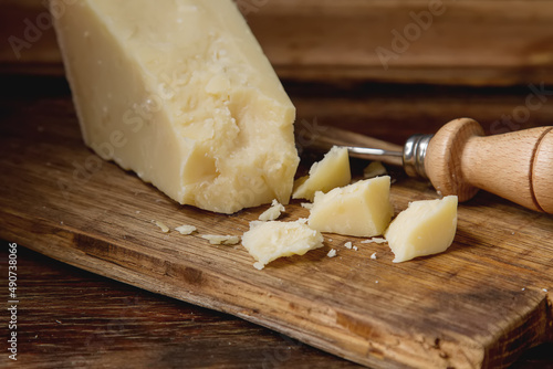 piece of Italian parmesan cheese with a knife. Dark wood background