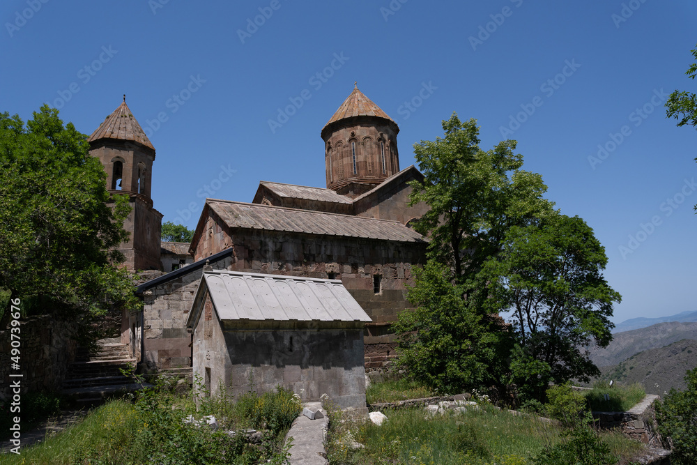 a large dark stone church high in the mountains of Georgia, next to which there are green trees and behind it a beautiful blue sky
