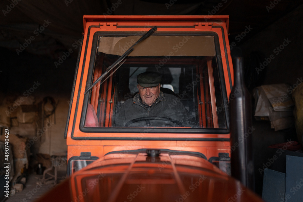 Smiling senior man siting in tractor in garage before work Smiling senior man siting in tractor in garage before work