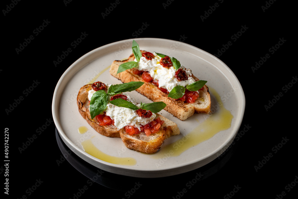 Two grilled bruschetta with stracciatella cheese and sun-dried tomatoes on black plate stand, top view, menu photography