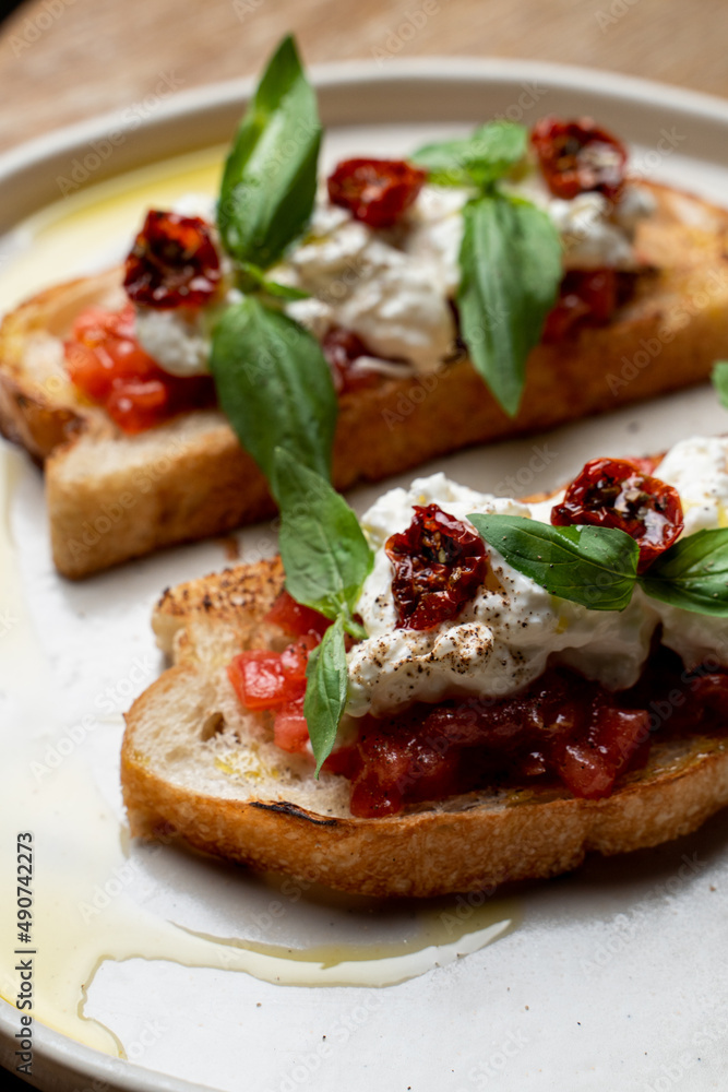 Two grilled bruschetta with stracciatella cheese and sun-dried tomatoes on black plate stand, top view, menu photography