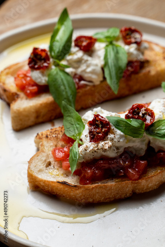 Two grilled bruschetta with stracciatella cheese and sun-dried tomatoes on black plate stand  top view  menu photography