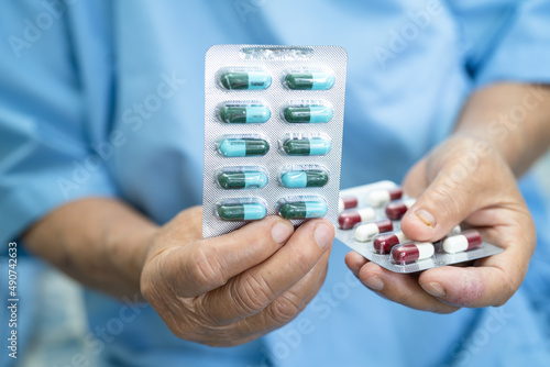 Asian senior or elderly old lady woman patient holding antibiotics capsule pills in blister packaging for treatment infection patient in hospital, Pharmacy drugstore concept. 