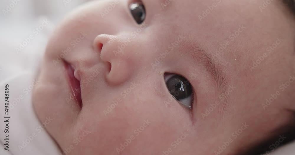 Close up macro portrait adorable newborn baby infant child girl face wakes up and opens his eyes looking at camera on the bed in the morning at home Close up macro portrait adorable newborn baby infant child girl face wakes up and opens his eyes looking at camera on the bed in the morning at home