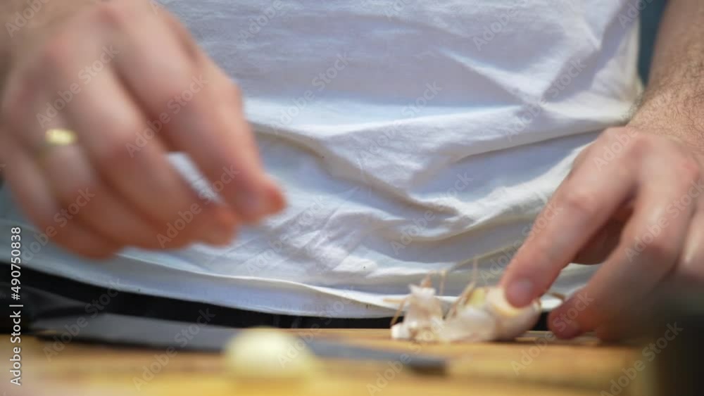 Hands of man in white t-shirt separating cloves of garlic on cutting board. man peels garlic standing at kitchen Hands of man in white t-shirt separating cloves of garlic on cutting board. man peels garlic standing at kitchen