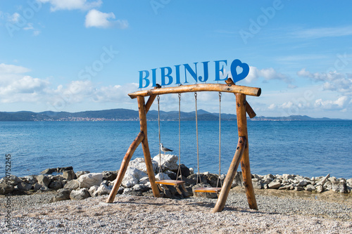 Fototapeta Naklejka Na Ścianę i Meble -  Beautiful coastal village Bibinje close to Zadar in Croatia, sign on the wooden swings on the beach with the view on the opposite island Ugljan