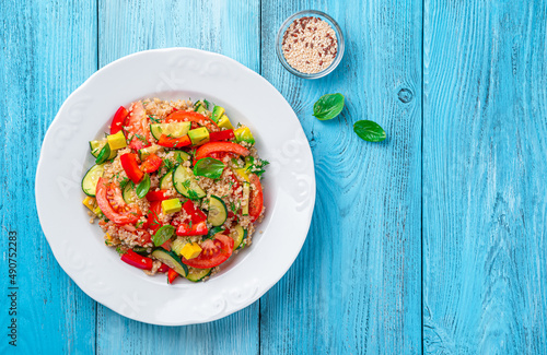 Tabbouleh salad with tomatoes, cucumber, red pepper, avocado and quinoa on a blue background.